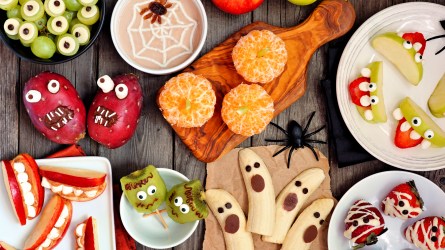 Healthy Halloween fruit snacks. Selection of fun, spooky treats. Top view table scene over a rustic wood background.