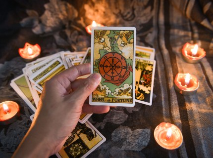 Hand holding tarot card with more tarot cards and candles in the background