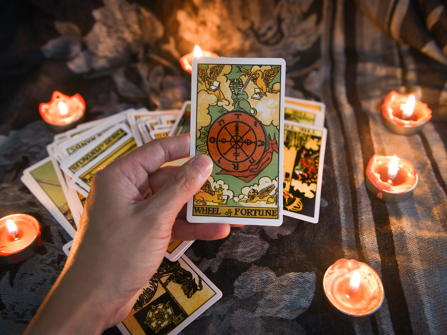 Hand holding tarot card with more tarot cards and candles in the background