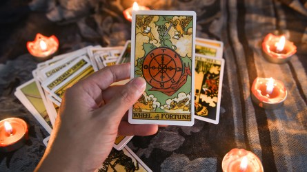 Hand holding tarot card with more tarot cards and candles in the background