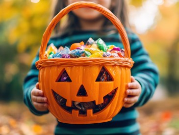 Little kid holding pumpkin basket filled with candy