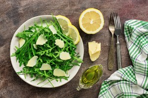 Light diet salad of arugula, parmesan and lemon on a dark rustic background. Top view, flat lay, copy space