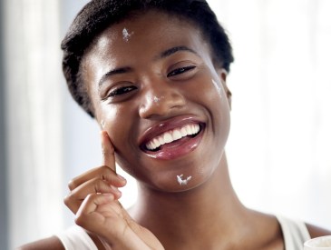 Skincare, cream and portrait happy woman in home, beauty cosmetics and self care in morning. Smile, lotion and skin product application for African model in bathroom for anti ageing facial treatment