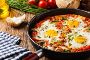 Shakshouka, dish of eggs poached in a sauce of tomatoes, chili peppers, onions. Front view.