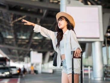 travel, business trip, people, gesture and tourism concept - smiling young woman waving hand and catching taxi at airport terminal or railway station; Away luggage dupes