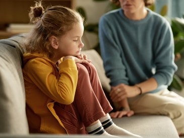 Little boy sitting on sofa without mood and having no desire to talk to his mom