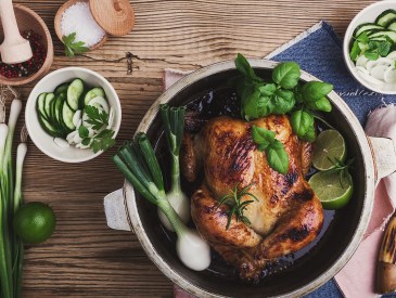 Homemade roasted chicken with green vegetables salad and fresh herbs on rural wooden table viewed from above