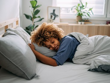 Black woman in pajamas napping in her bed at home.