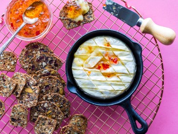 A baked brie in a cast iron fry pan served with crackers and red pepper jelly, ready for snacking.