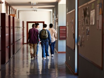 Full length rear view of male teenage students walking by lockers in corridor at high school